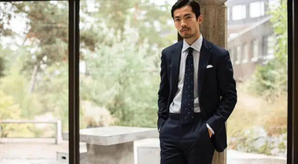Man i mörk kostym med prickig slips, en stil som påminner om modern japan fashion.