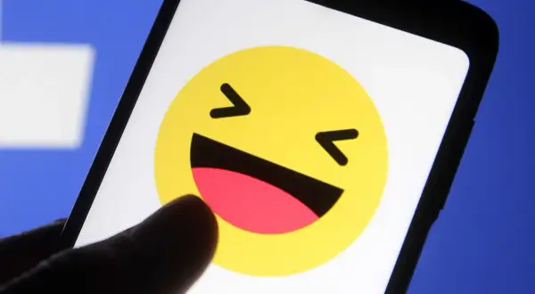 En tumme pekar på en skrattande emoji på en mobilskärm. Kanske undrar du vad betyder lol?