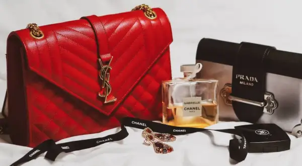 En röd, quiltad modalu väska med gulddetaljer, bredvid en Prada-väska, Chanel-parfym och smycken.