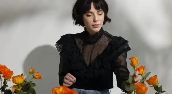 En kvinna med en elegant french bob, klädd i en svart spetsblus, omgiven av orange rosor.
