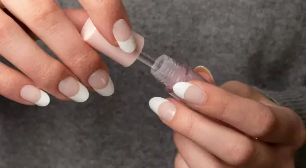 Händer med franska manikyr, vita naglar och en rosa nagellacksflaska.