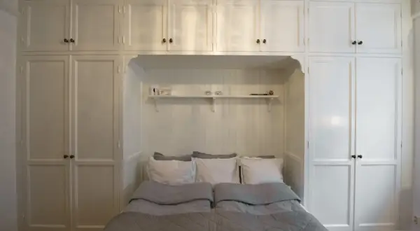 En inbäddad säng med grå täcken och vita kuddar, omgiven av vita skåp som utstrålar en tidlös, old money aesthetic.