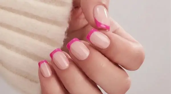 En hand med naglar i fransk manikyr med en modern twist av knallrosa. Olika nail types som visar en lekfull stil.
