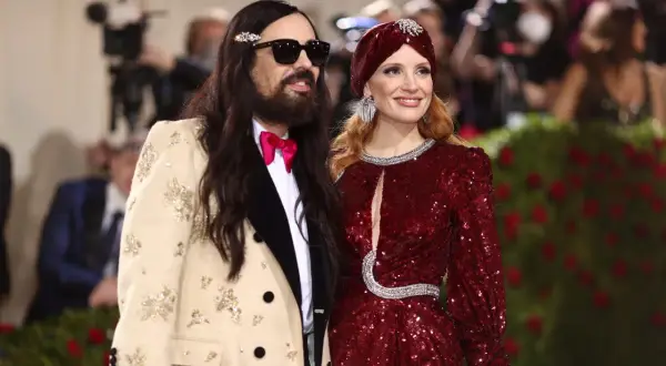 Alessandro Michele och Jessica Chastain poserar glatt. Han bär en beige kavaj med broderier och en rosa fluga.
