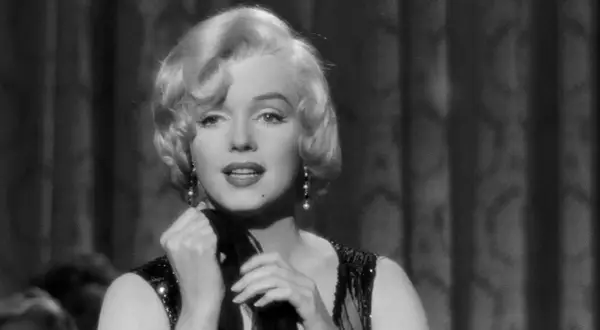 Marilyn Monroe i en ikonisk scen från en klassisk film. Hennes blonda lockar, pärlörhängen och glittriga klänning fångar blicken.