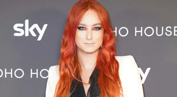 Harris Reed med flammande rött hår och dramatisk makeup, klädd i en vit kavaj.