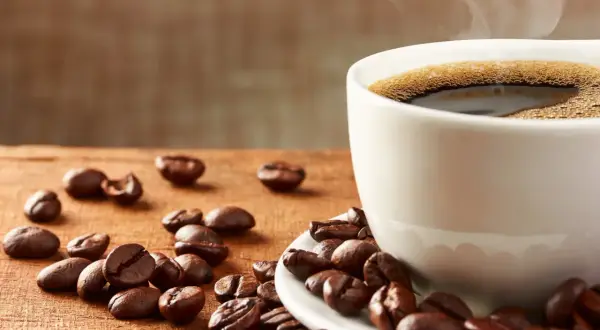 En kopp ångande kaffe med bönor utspridda på träbordet. Frank Hu älskar morgonkaffe.