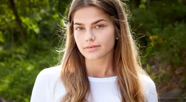En ung kvinna med blont hår och blå ögon, en blivande top model Sverige, ler mot kameran utomhus.