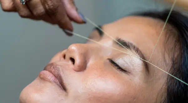 En tråd dras över ögonbrynet för att forma det, en klassisk brow bar-behandling som ger en perfekt brow bar mood.