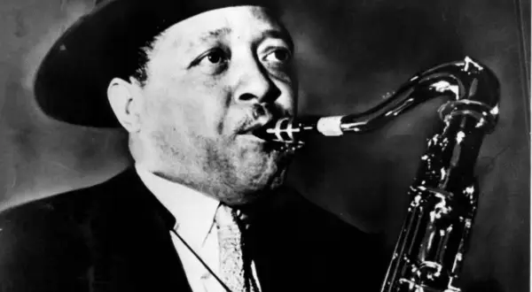 En man med hatt spelar saxofon. Hans musik är så cool, en riktig synonym för jazzens själ.