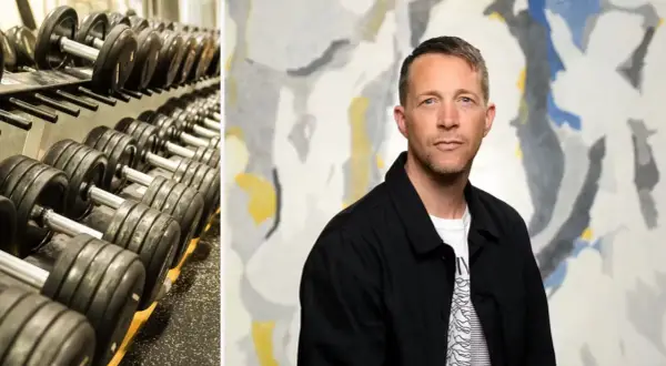 En man med en blick som antyder "looksmaxxing meaning" står framför en abstrakt tavla. Till vänster syns en hylla med hantlar.