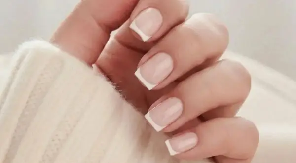 En hand med klassisk fransk manikyr på korta naglar, insvept i en mjuk, beige tröja.