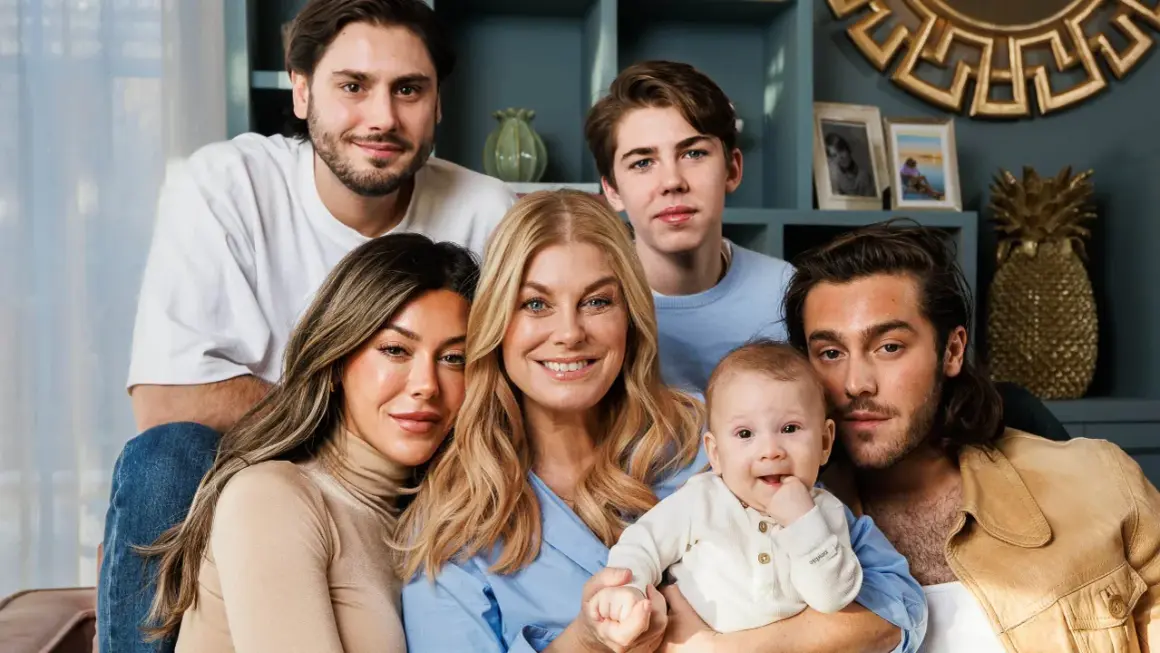 Familjen samlad, med en leende mamma som håller sitt luciano ingrosso barn. Två äldre söner och en ung man ler mot kameran.