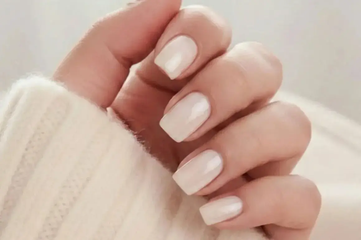 En hand med ljusa, mandelformade naglar i en mjuk, krämig färg. Perfekt almond nails inspo för en elegant look.