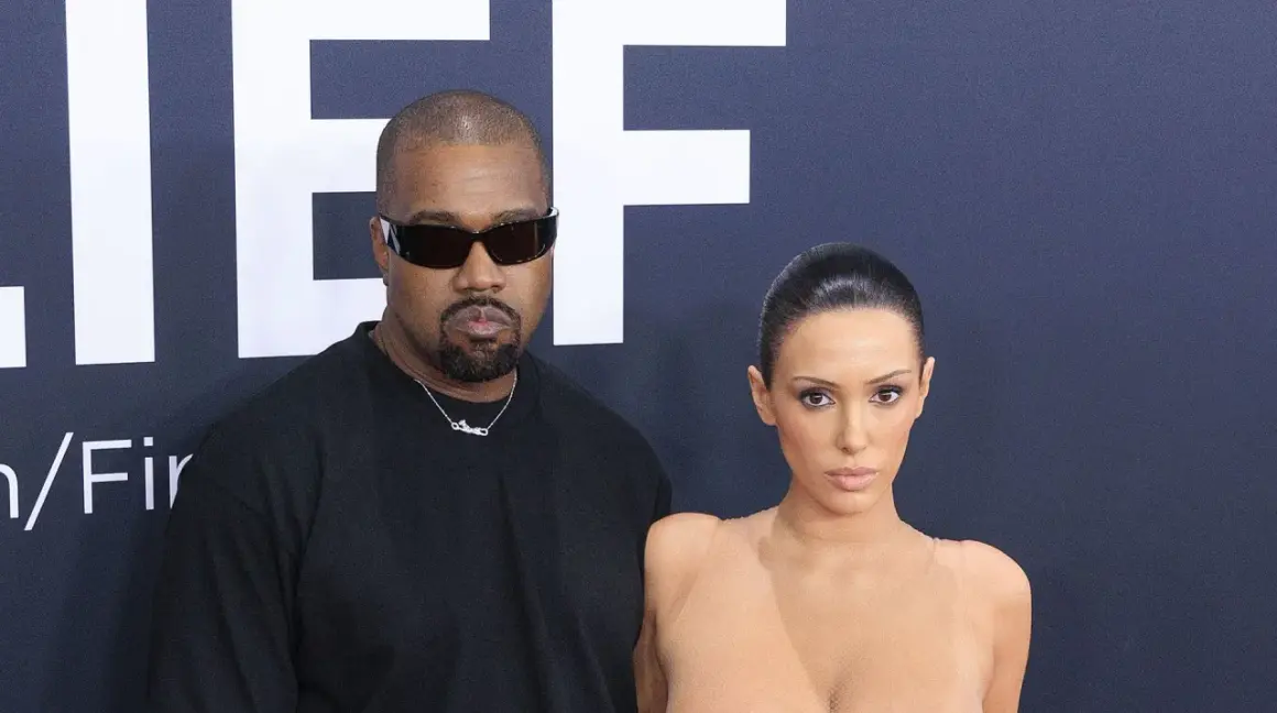 Kanye West och Bianca Censori poserar framför en stor logotyp.