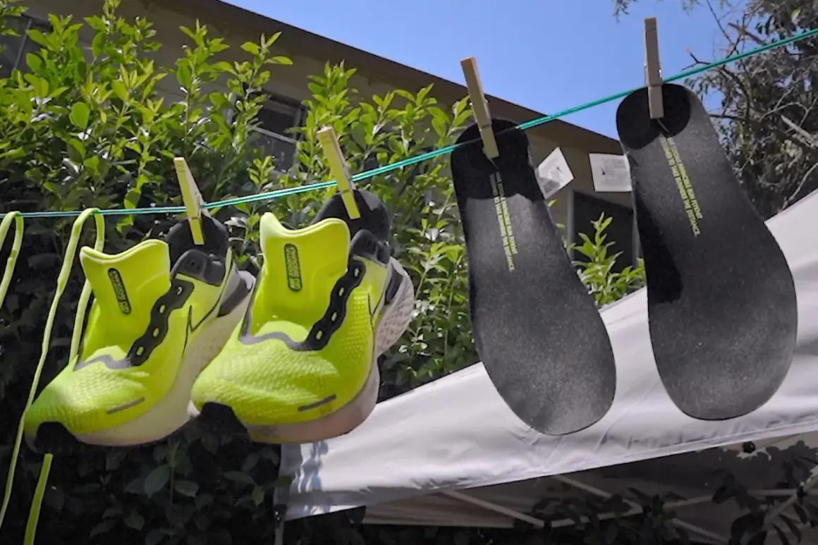Två par neongröna löparskor och två svarta innersulor hänger på tork. Nike Move to Zero-filosofin syns i detaljerna.