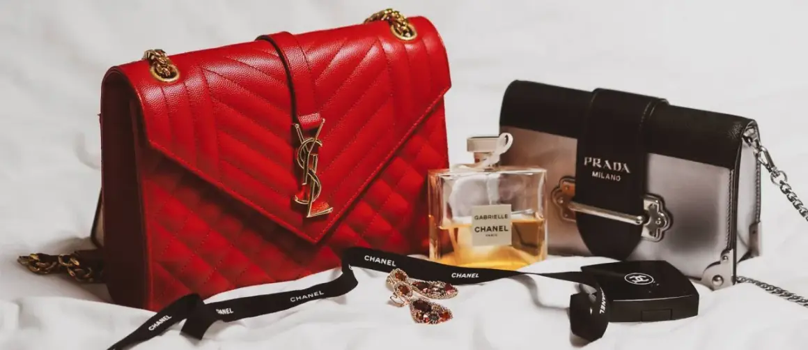 En röd, quiltad modalu väska med gulddetaljer, bredvid en Prada-väska, Chanel-parfym och smycken.