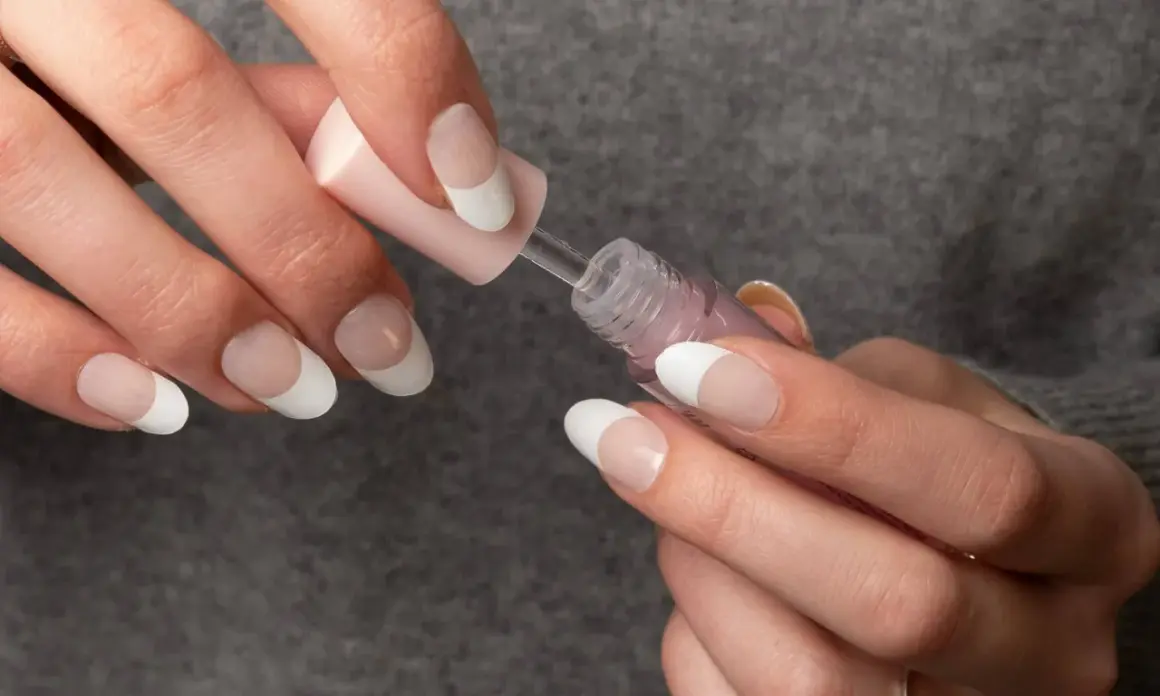Händer med franska manikyr, vita naglar och en rosa nagellacksflaska.