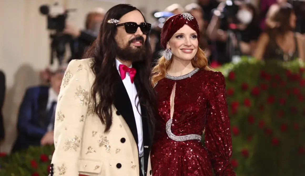 Alessandro Michele och Jessica Chastain poserar glatt. Han bär en beige kavaj med broderier och en rosa fluga.