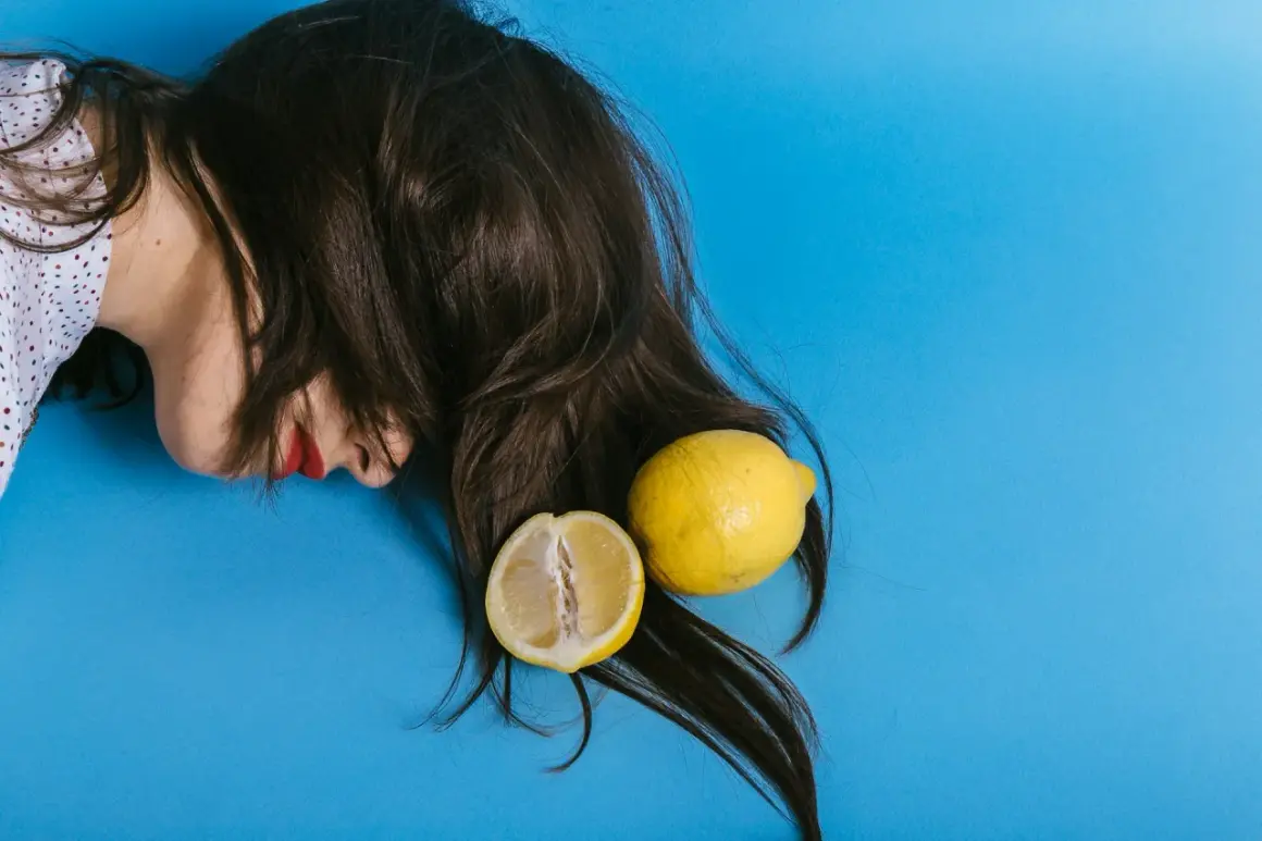 En person med mörkt hår och röda läppar ligger på en blå bakgrund med en hel och en halv citron. Kanske en idé för att bleka håret med citron?