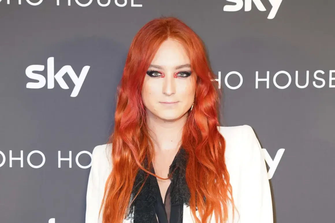 Harris Reed med flammande rött hår och dramatisk makeup, klädd i en vit kavaj.