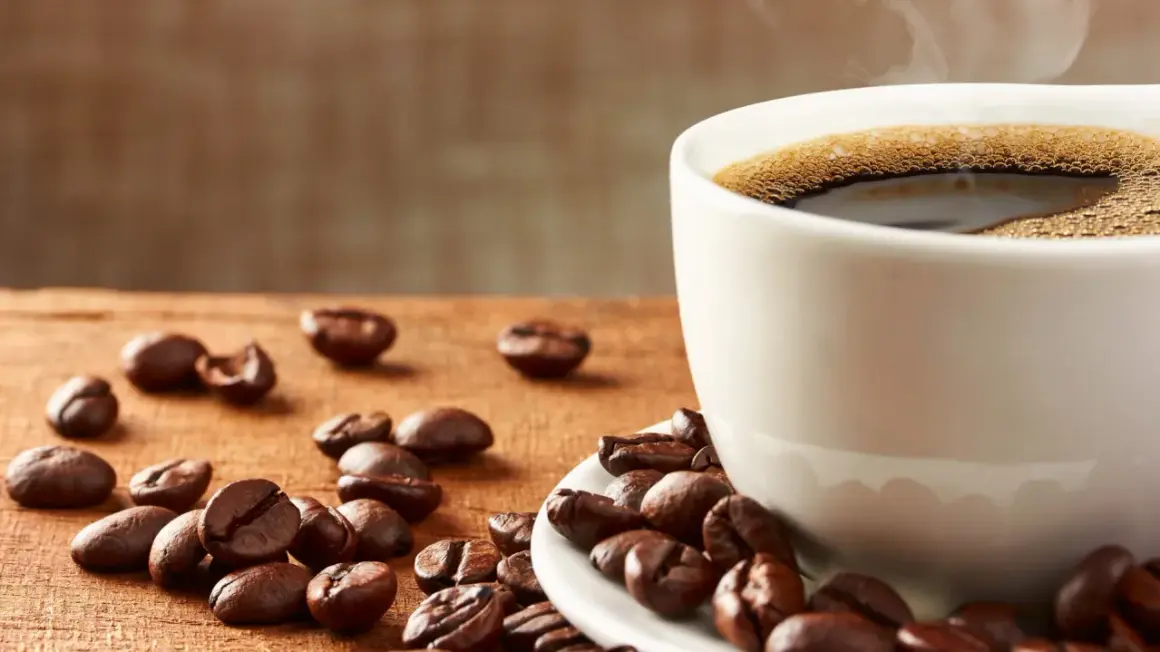 En kopp ångande kaffe med bönor utspridda på träbordet. Frank Hu älskar morgonkaffe.