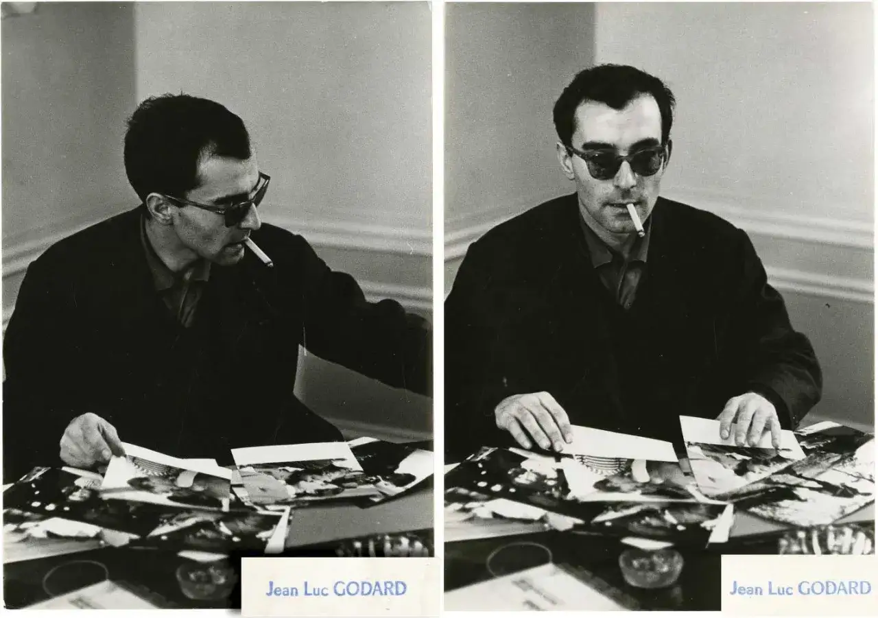 Jean-Luc Godard, med solglasögon och cigarett, bläddrar bland bilder, kanske för sina filmer.