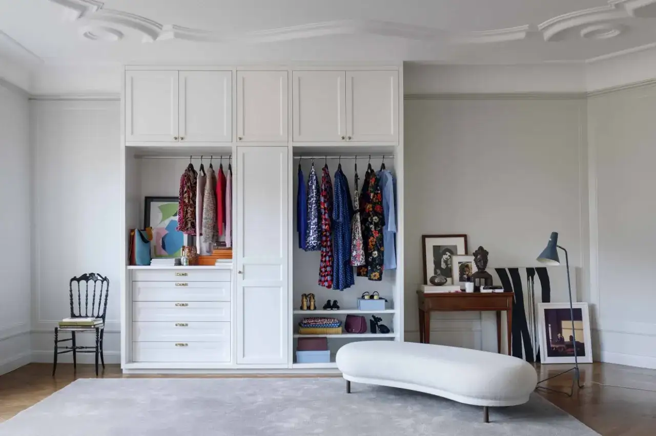 En vit garderob med färgglada kläder som speglar en personlig stil. En stol och en soffa bidrar till rummets charm.