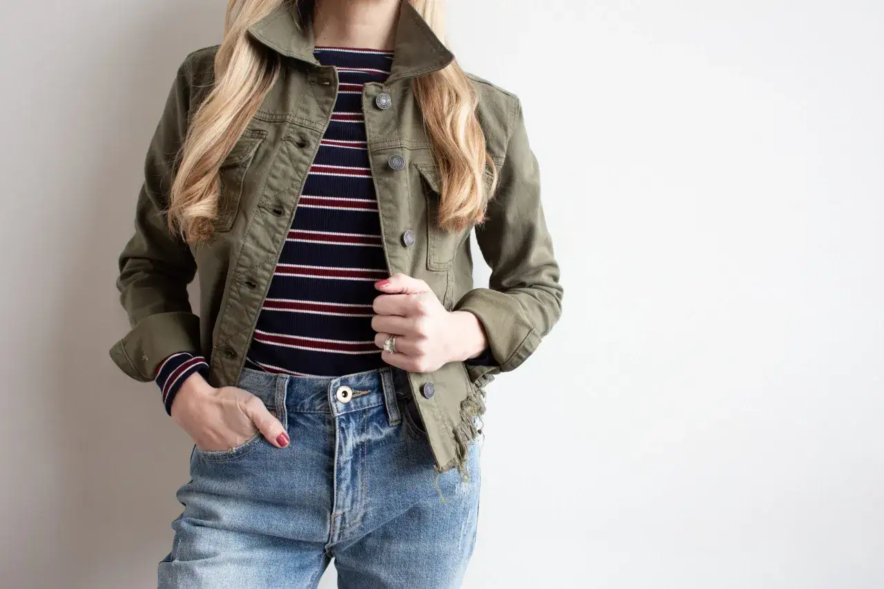 En kvinna i en gr&ouml;n jacka och randig topp, redo f&ouml;r v&aring;rmode 2026 dam. Jeans och en avslappnad stil.
