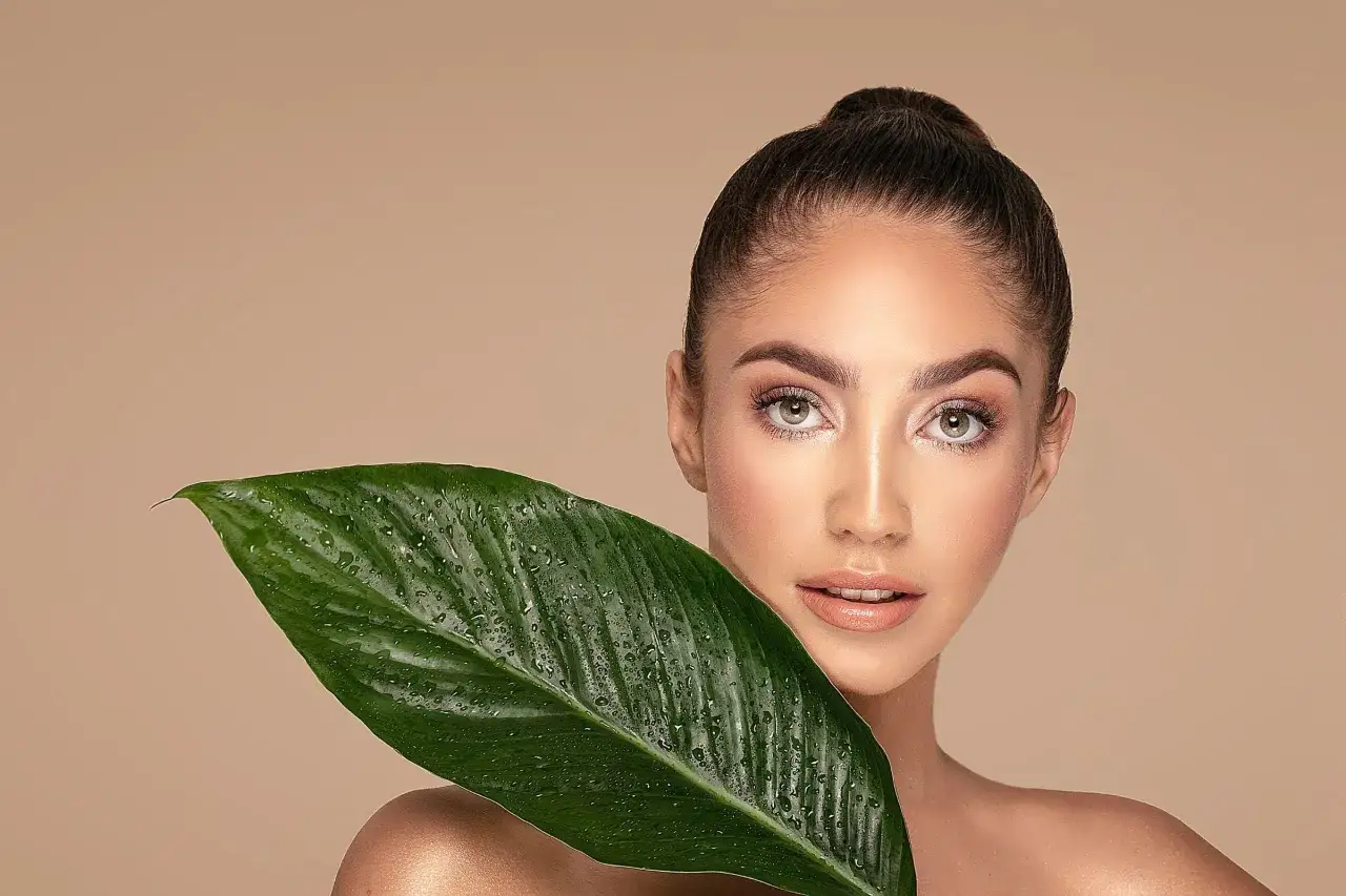 En kvinna med en grön, vattendroppad blad som täcker en del av hennes ansikte. Naturlig skönhet och enkla beauty hacks.
