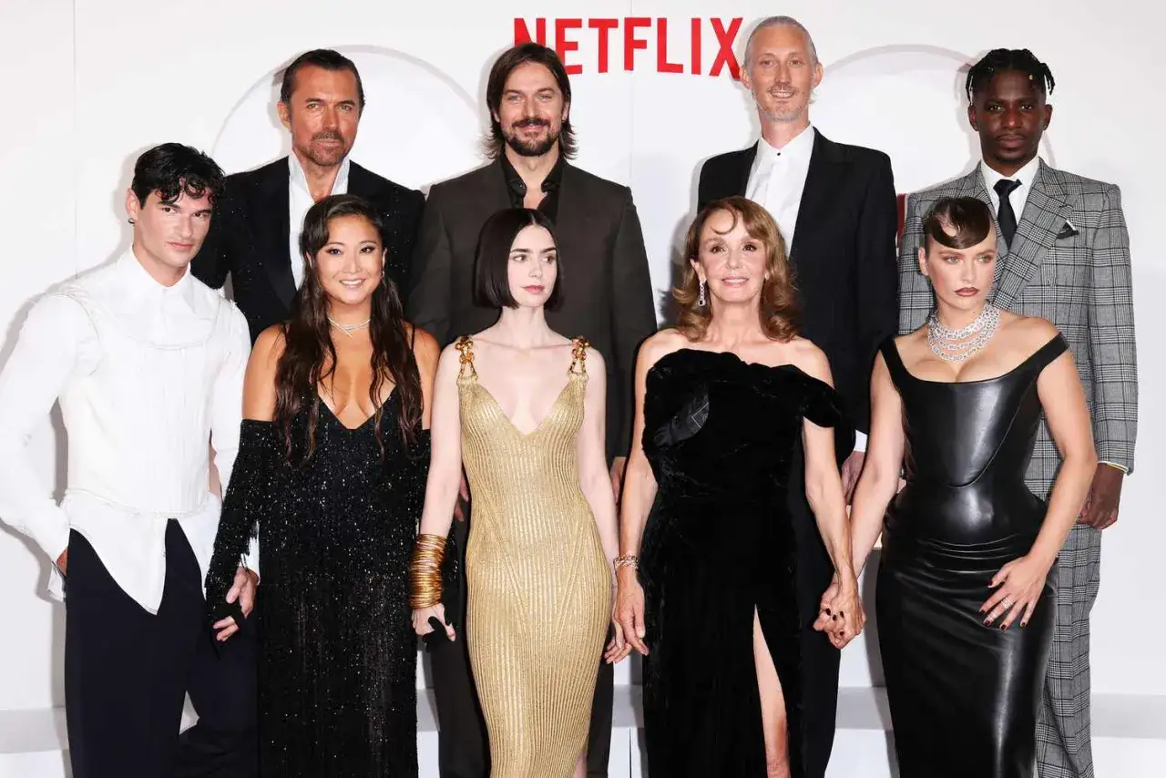 Här är rollistan i Emily i Paris, samlad för ett Netflix-evenemang. Skådespelarna poserar glatt framför en vit bakgrund.