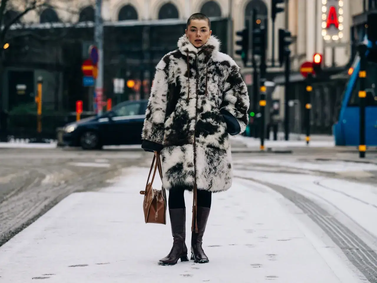 En person med kortklippt hår bär en fluffig pälsjacka och stövlar i snön under cph fashion week.