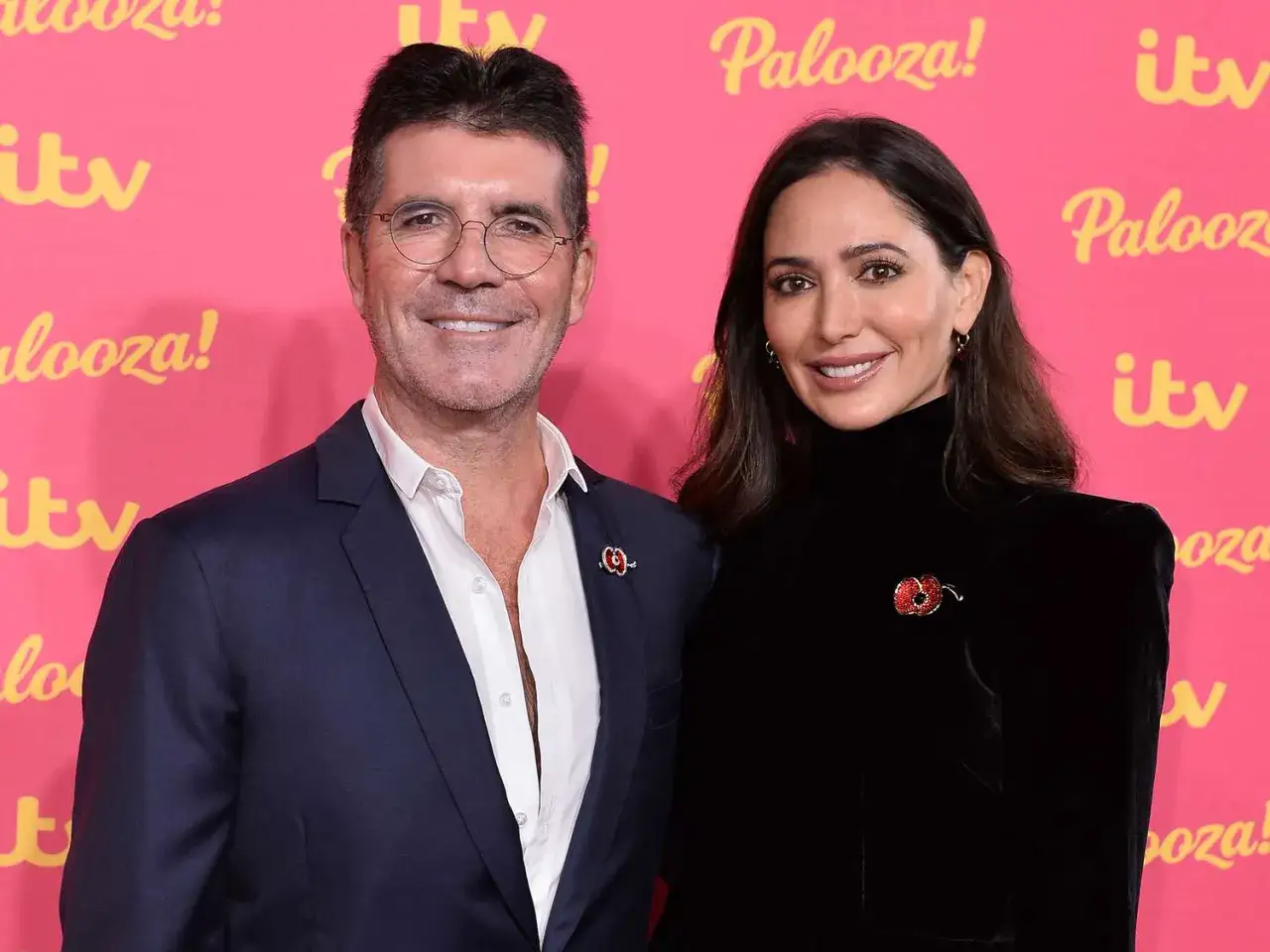 Simon Cowell och Lauren Silverman ler mot kameran på en rosa bakgrund med