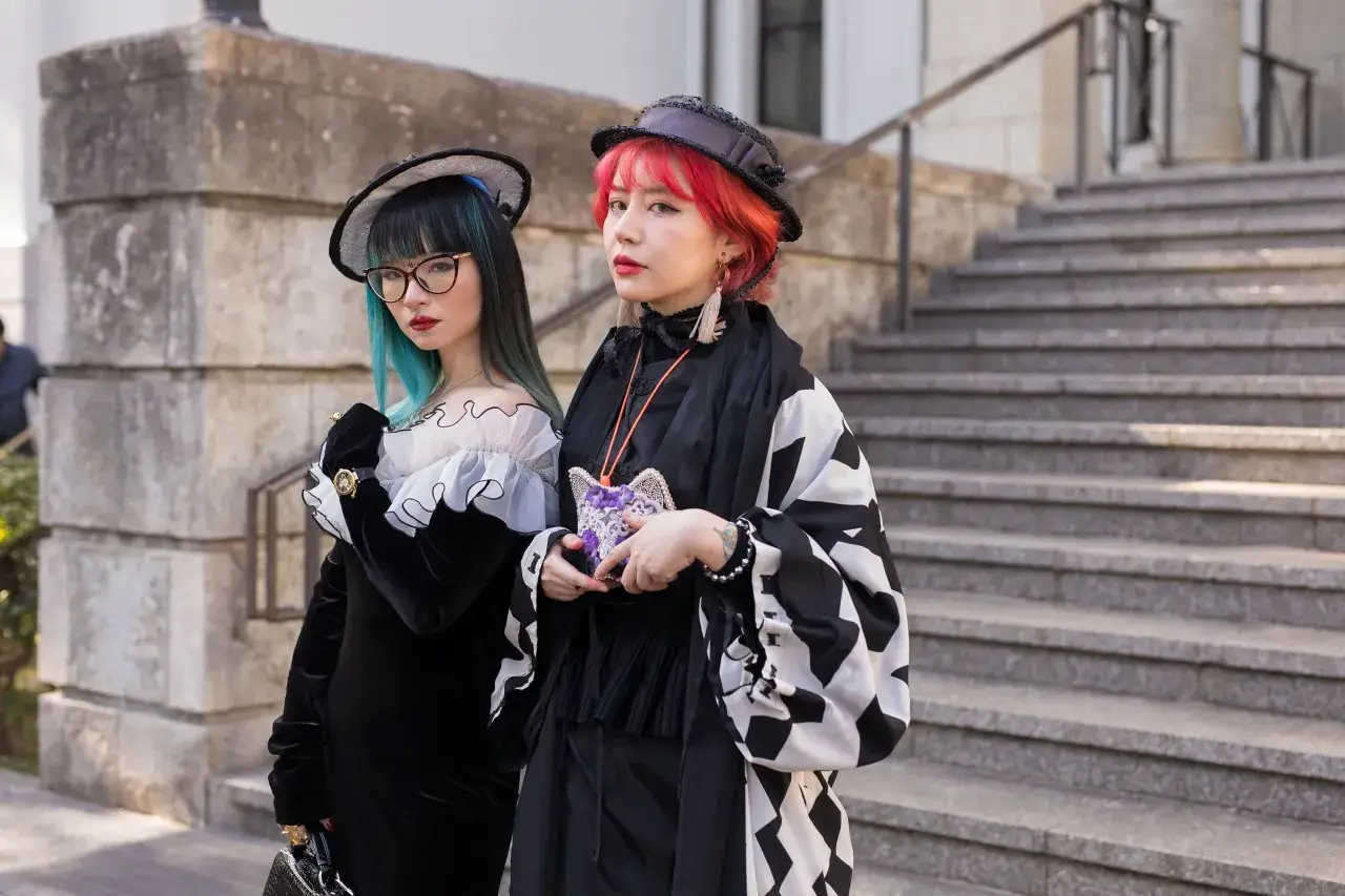 Två unga kvinnor med färgglatt hår och unik japan fashion-stil poserar framför en stenbyggnad.