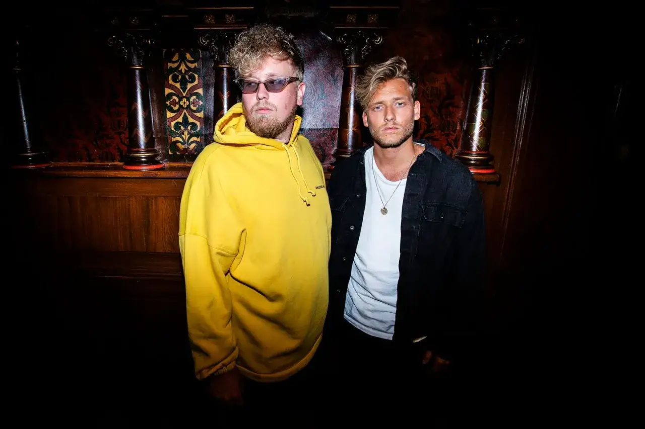 Sonny Fahlberg och en vän poserar i en mörk miljö med träpaneler och utsmyckade pelare.