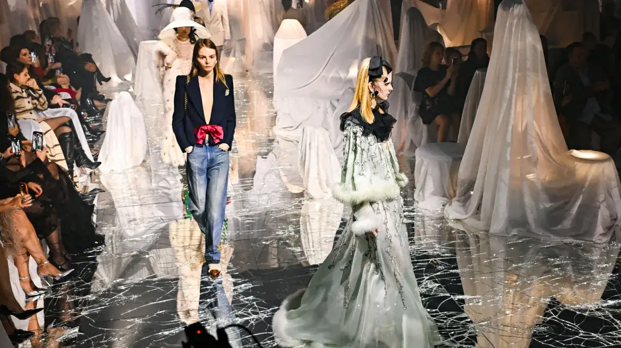 Modell på catwalken i en Alessandro Michele-inspirerad design, med publik som tittar på.
