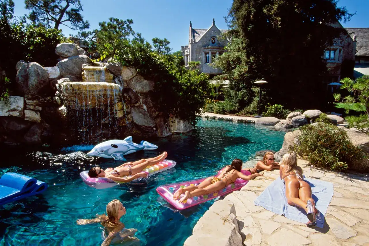 Solig dag vid poolen med vattenfall, delfinflotte och kvinnor som solar vid Playboy Mansion.