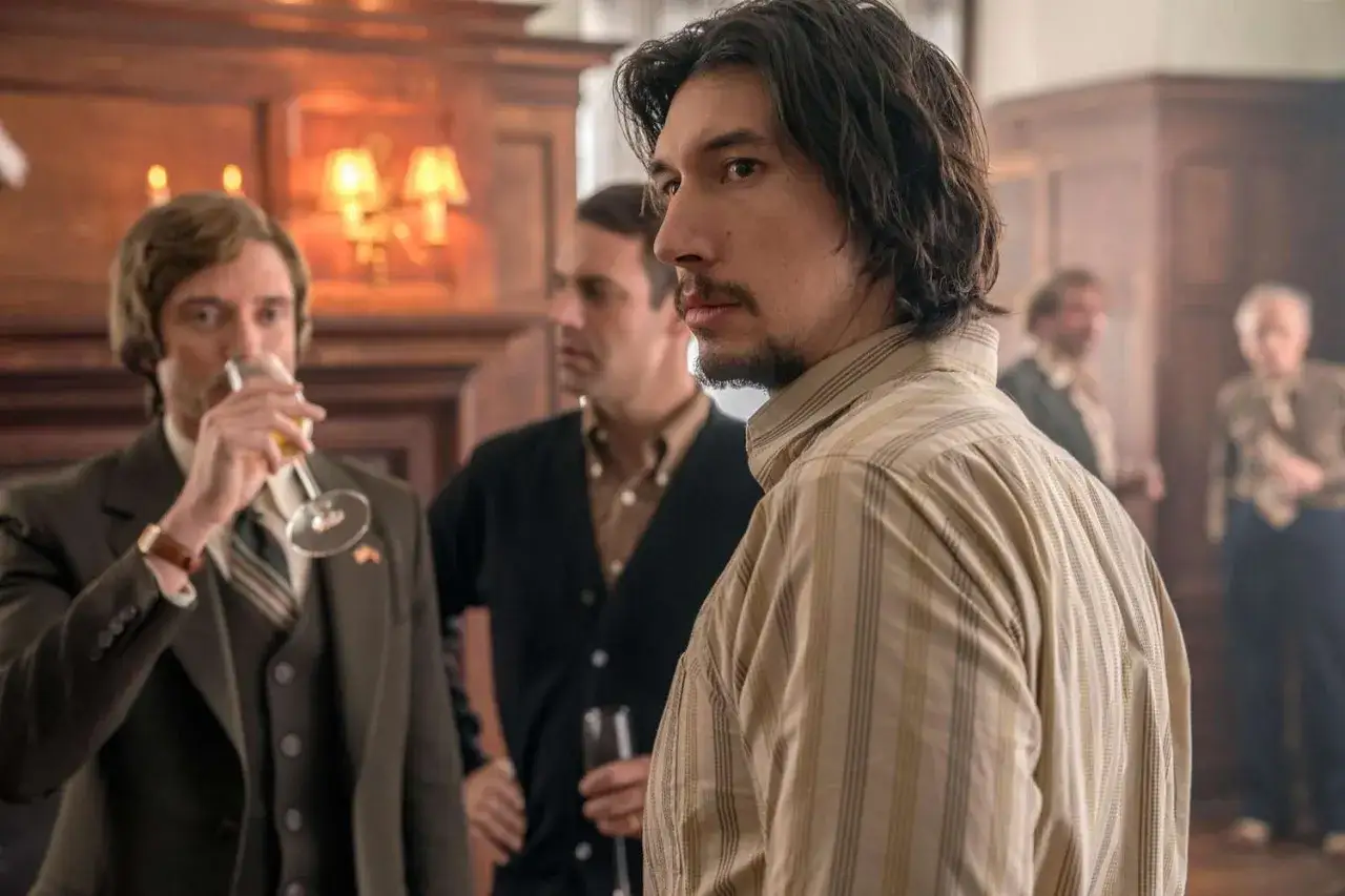 Adam Driver i en randig skjorta, med män i bakgrunden. En scen från filmer med Adam Driver.