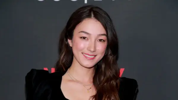 Natasha Liu Bordizzo ler glatt i en svart klänning med puffärmar.