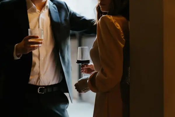 En man i kostym håller ett glas whisky, en kvinna i klänning håller ett glas rödvin. Kanske är det dags för några frågor till killar?