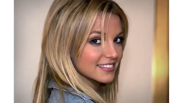 Britney Spears, med sitt ikoniska blonda hår, ler mot kameran. Hon påminner om tiden då hon släppte "Baby One More Time".