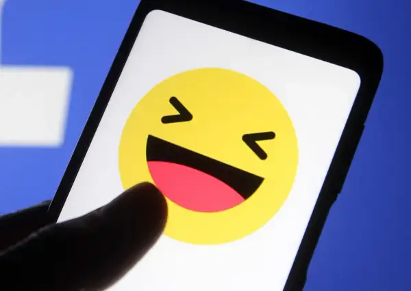 En tumme pekar på en skrattande emoji på en mobilskärm. Kanske undrar du vad betyder lol?