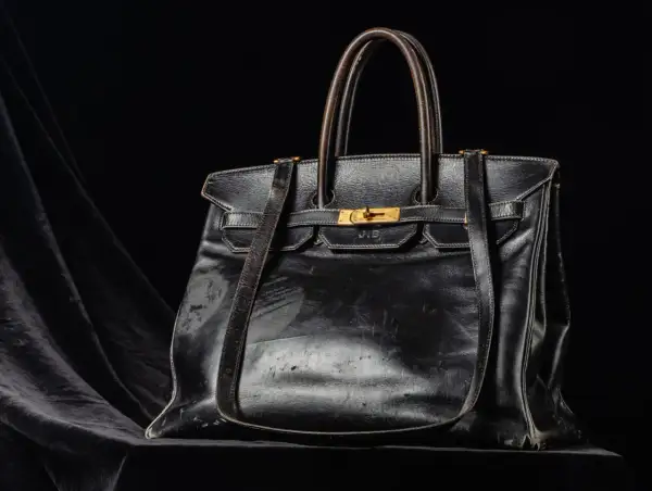 En svart, sliten läderväska i jane birkin style, med guldfärgade detaljer och initialerna J.B. präglade.