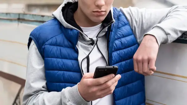 Ung kille med blå dunjacka och grå hoodie kollar på sin mobil. Kanske undrar han vad betyder simp?