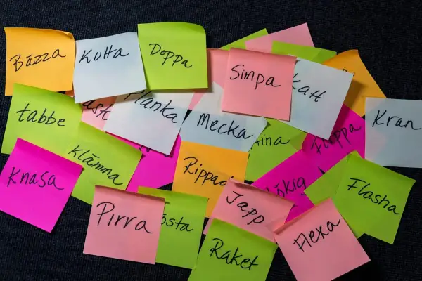Färgglada post-it-lappar med ord som "Bázza", "Kuta", "Doppa", "Simpa", "Planka", "Mecka", "Rippac", "Japp", "Raket", "Flasha", "Flexa" och "Kran". Kanske en ordlek eller en synonymlista för skvaller?