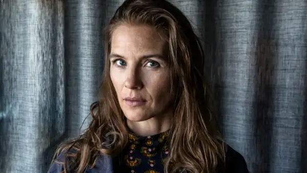 Lisa Carlehed, med blå ögon och brunt hår, blickar intensivt mot kameran. Hon bär en mörkblå jacka över en mönstrad tröja.