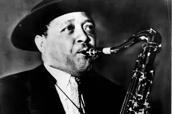 En man med hatt spelar saxofon. Hans musik är så cool, en riktig synonym för jazzens själ.